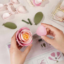 Een persoon is de Robotime Pink Camellia aan het bouwen