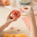 Een persoon is bezig met de bloem van de Robotime Pink Dahlia te knutselen