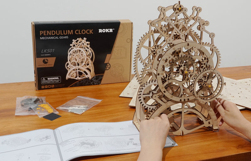 Sfeerfoto van de voltooide Robotime Pendulum Clock met inhoud van de verpakking en doos op de achtergrond